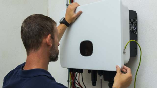 A person adjusts a white electrical unit mounted on a wall, with colorful wires visible.