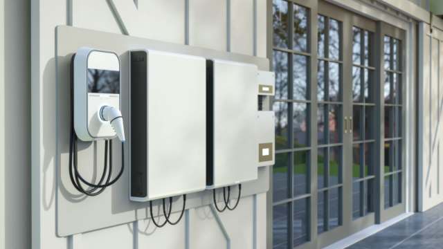 An electric vehicle charging station mounted on an exterior wall beside large glass doors.