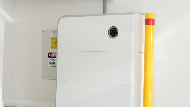 A white machine with a round sensor next to a warning sign about toxic fumes and a yellow safety post.