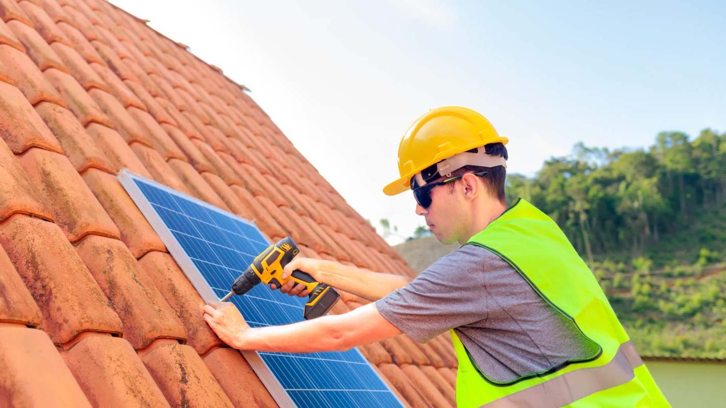 A person installs a solar panel on a tiled roof using a drill.