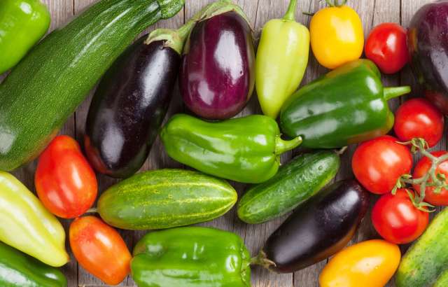 A variety of colorful vegetables including zucchini, peppers, tomatoes, and cucumbers on a wooden surface.