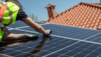 A person in a reflective vest adjusts solar panels on a rooftop.
