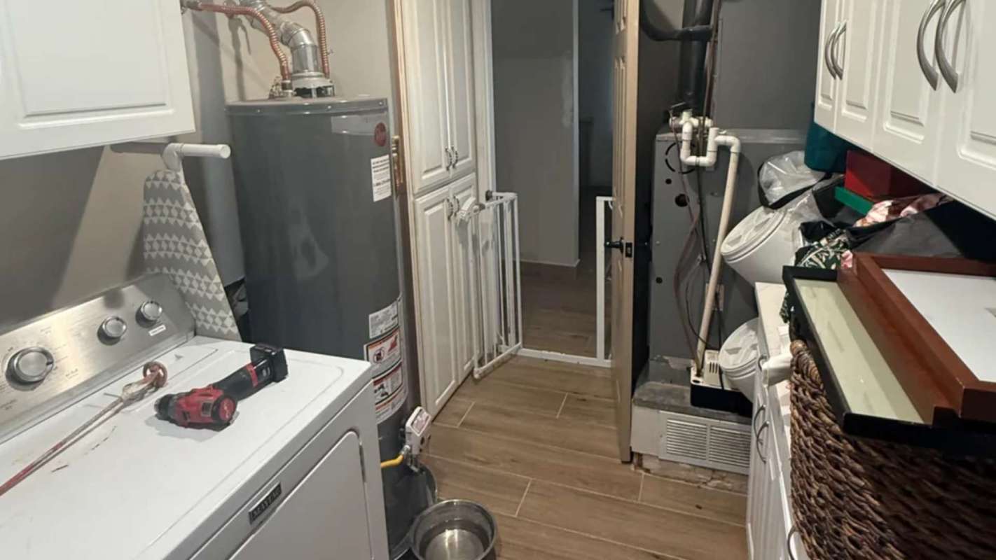 A laundry room featuring a washing machine, water heater, and various storage items.
