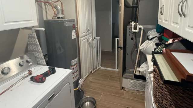 A laundry room featuring a washing machine, water heater, and various storage items.
