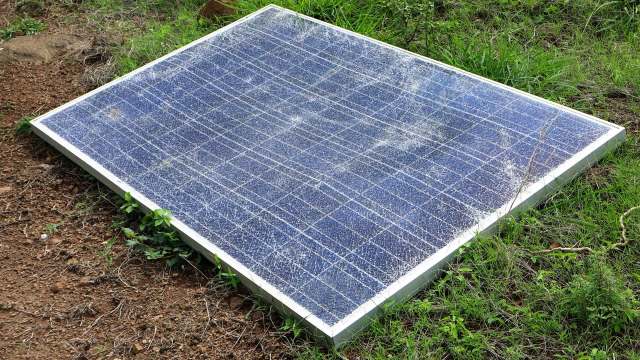 A solar panel situated on the ground surrounded by grass and dirt.