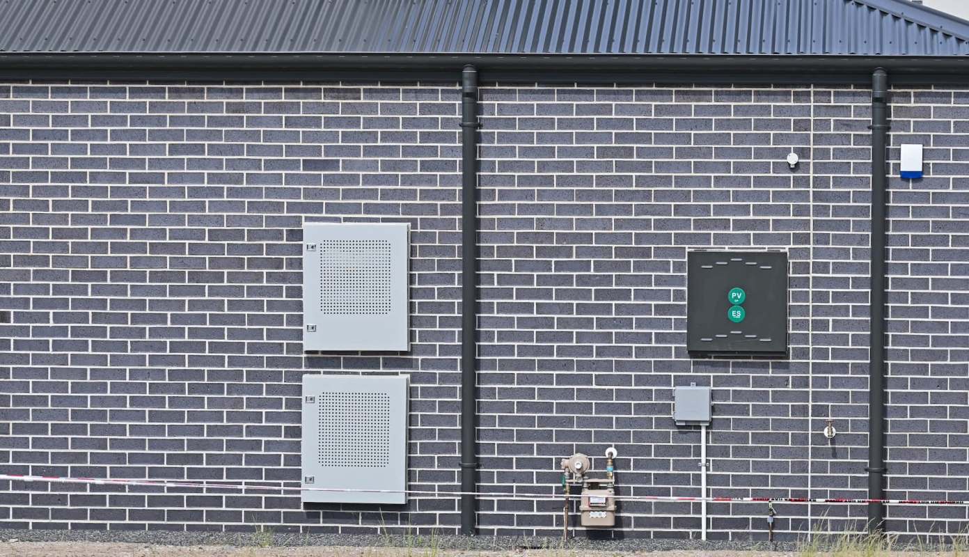 A gray brick wall with two utility boxes and a gas meter attached.