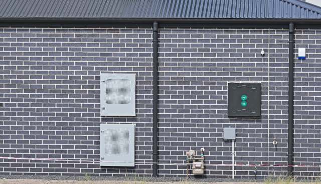 A gray brick wall with two utility boxes and a gas meter attached.