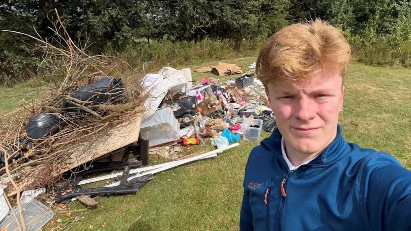 A person stands in front of a large pile of discarded trash and debris in an outdoor area.