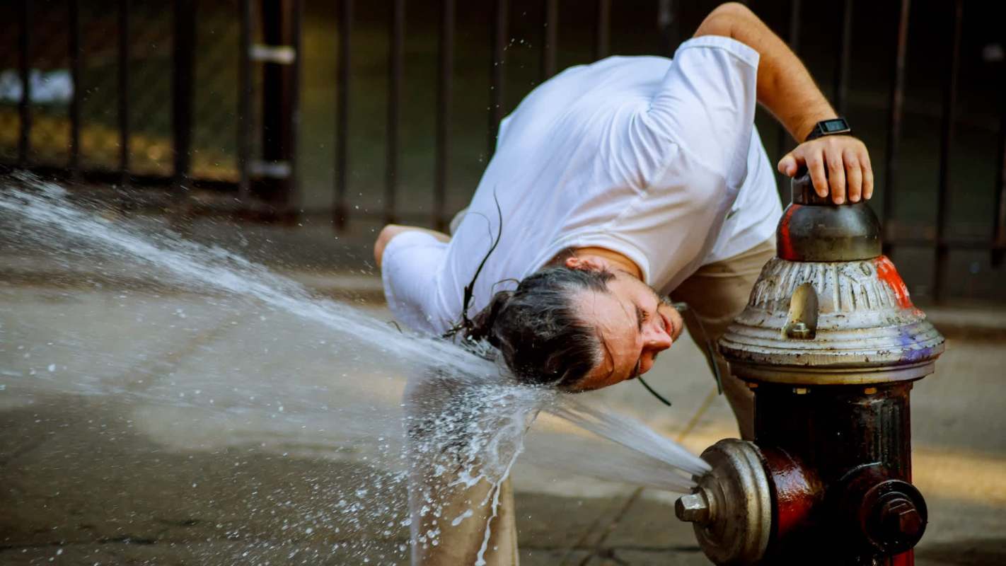 A man leans over a fire hydrant with water spraying upward.