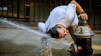 A man leans over a fire hydrant with water spraying upward.
