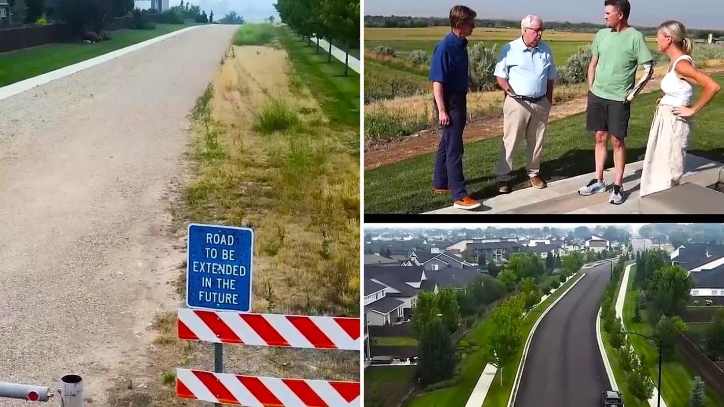 A sign indicating "Road to be extended in the future" beside a gravel road and a group of people discussing in a landscaped area.