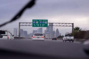Highway sign indicating directions for I-10, I-59, and I-69 with a city skyline in the background.