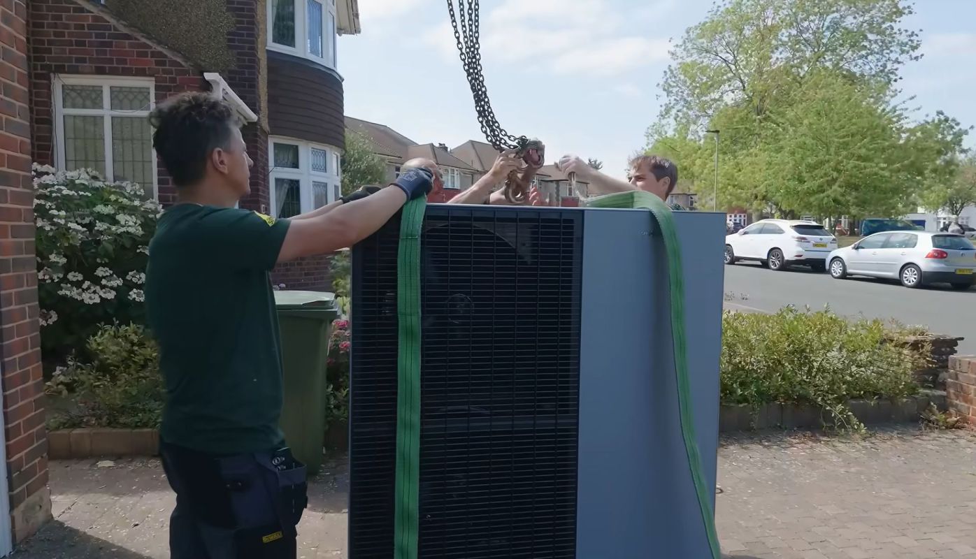 Three people hooking a heat pump to a crane.