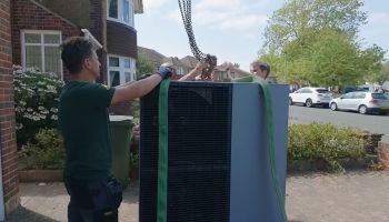Three people hooking a heat pump to a crane.
