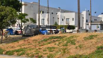 A group of tents and homeless individuals near a building with a sign for Project Youth Inc.