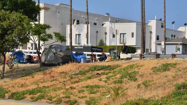 A group of tents and homeless individuals near a building with a sign for Project Youth Inc.