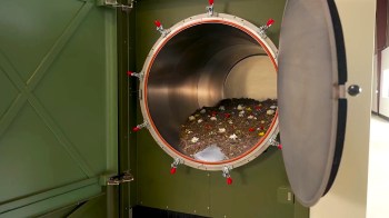 An open composter with soil and scattered flower petals inside.
