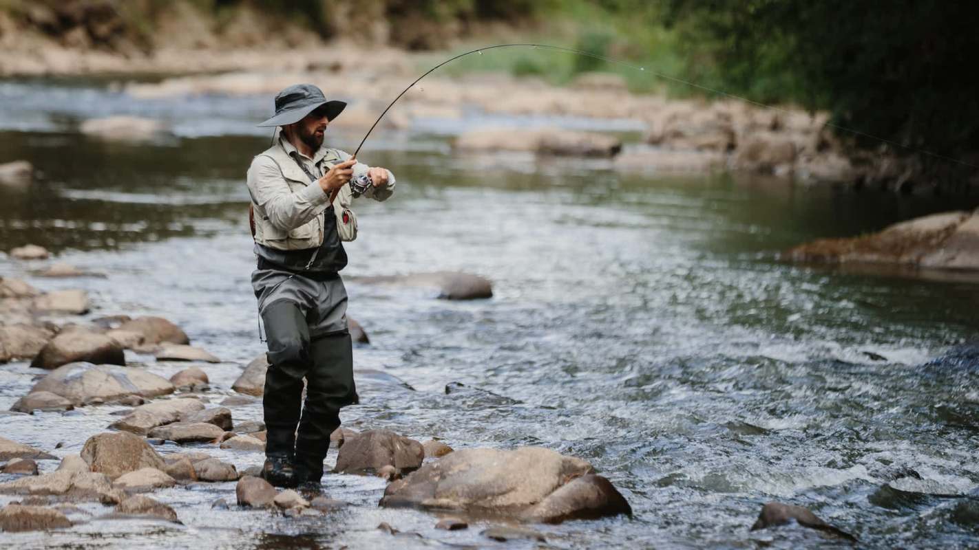 A man fishing in a river while standing on rocky ground.