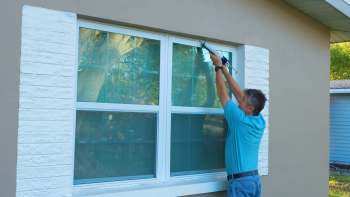 A person applies caulk around a window frame on a house.