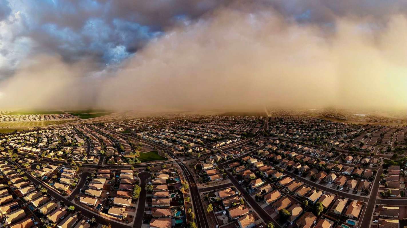 Aerial view of a suburban neighborhood with a dust storm approaching in the distance.