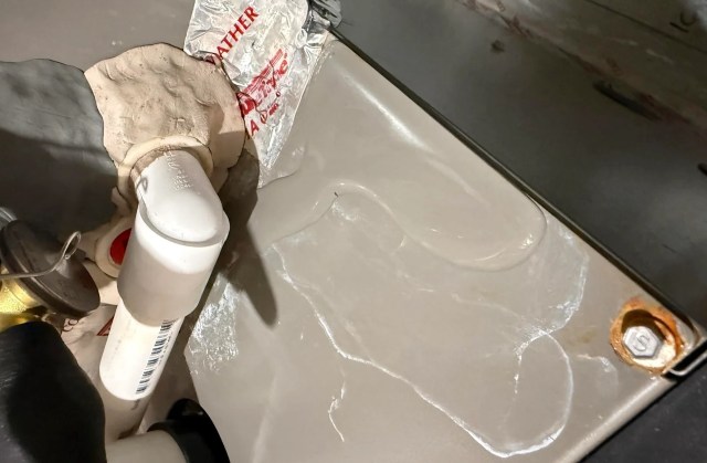 A white PVC pipe with sealant applied, surrounded by tools and materials in a work area along with a puddle of water.