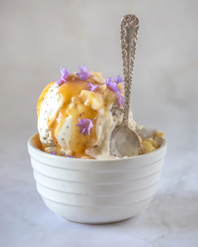 Ice cream in a dish with purple flowers and an orange sauce.
