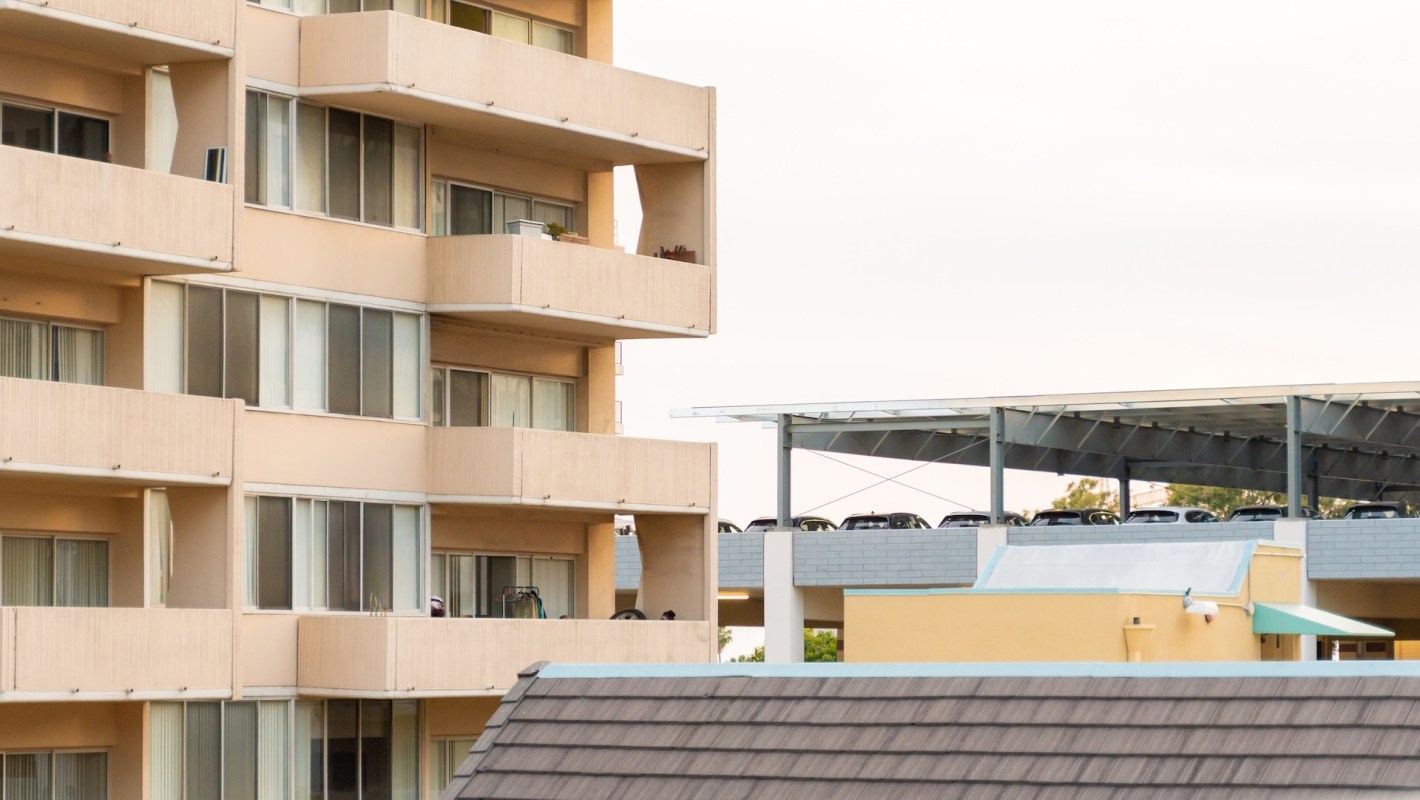 An apartment building with balconies and a parking structure with cars on the roof.