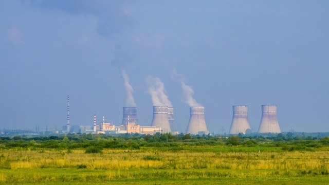 A nuclear power plant with cooling towers emitting steam, set against a green landscape.