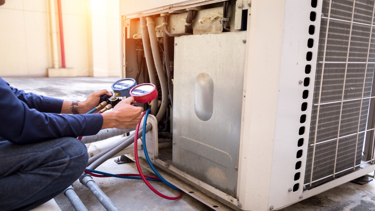 A person checks the pressure gauges on an air conditioning unit outdoors.