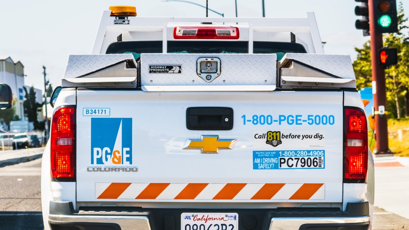 A PG&E service truck with safety signage parked at a traffic light.