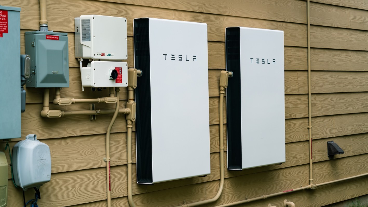 Two Tesla Powerwall energy storage systems mounted on a wall beside electrical equipment.