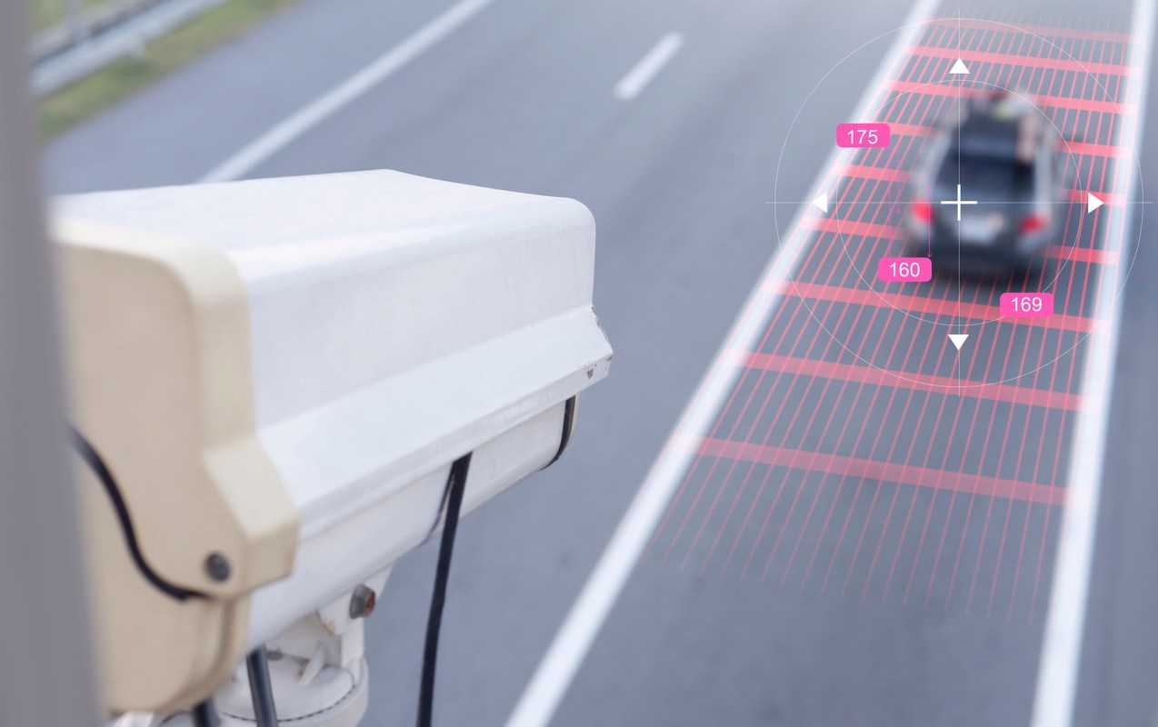 A traffic camera monitors a moving car on a road with speed detection graphics.