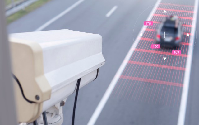 A traffic camera monitors a moving car on a road with speed detection graphics.