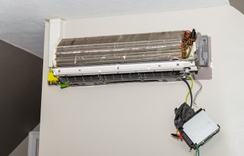 A mini-split air conditioning unit mounted on a wall with visible internal components and wiring.