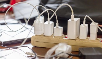 A power strip with multiple phone chargers and cables on a wooden surface.
