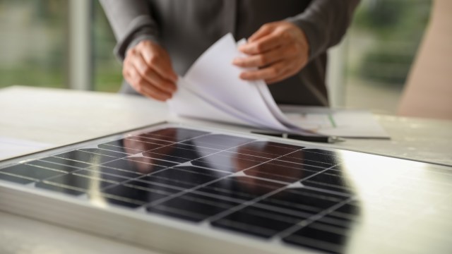 A person handles documents next to a solar panel on a table.