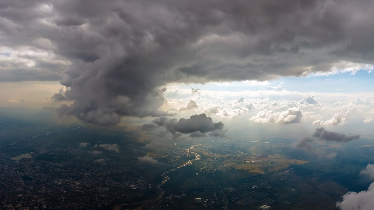 Aerial view of a landscape beneath a cloudy sky with patches of sunlight breaking through.