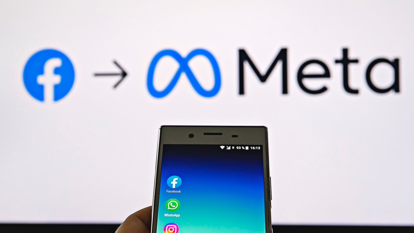 A smartphone displays social media app icons in front of a screen showing the logos for Facebook and Meta.