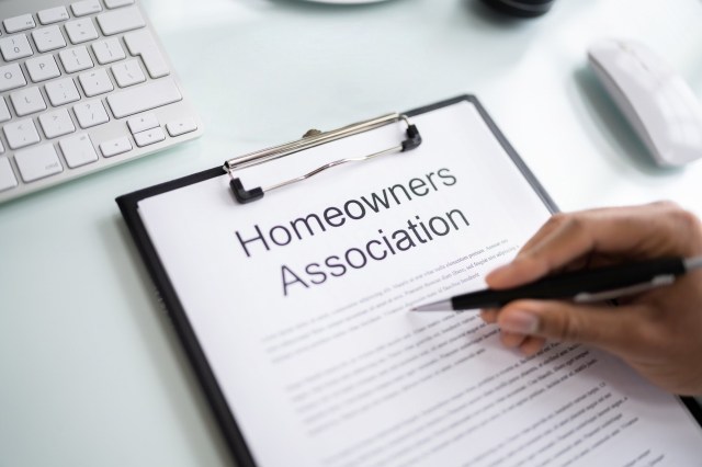A hand holding a pen is positioned over a clipboard with a document titled "Homeowners Association."