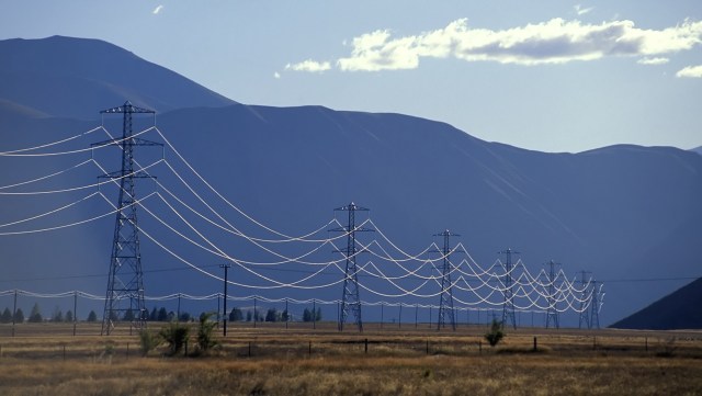 Power lines stretch across a flat landscape with distant mountains under a clear sky.