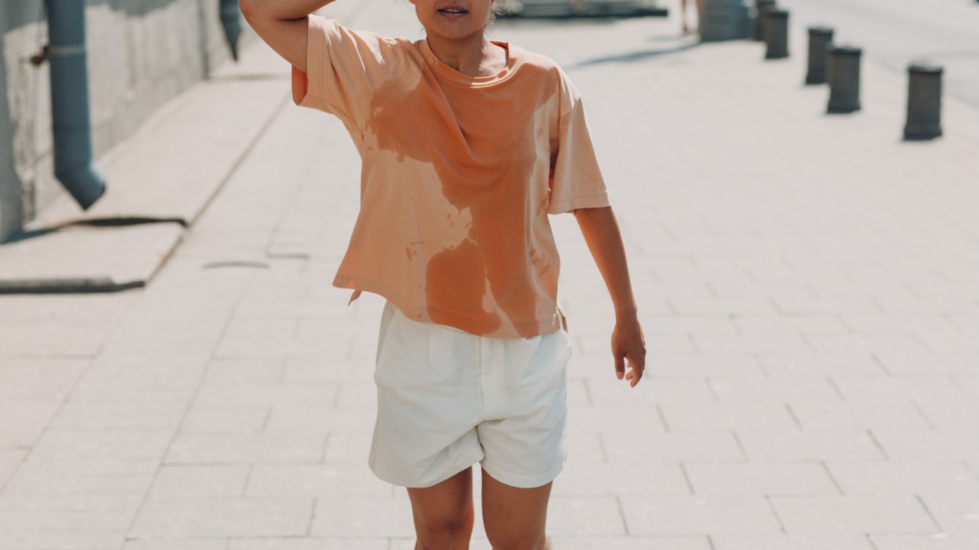 A person wearing a damp orange shirt and white shorts walks along a brick-paved street.