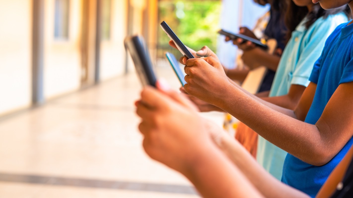 A group of children holding smartphones in a school hallway.