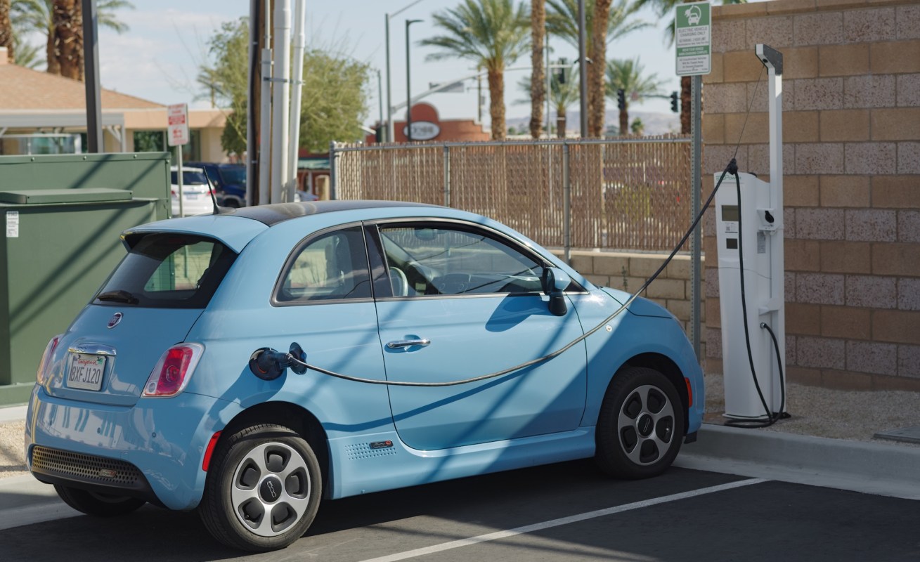 A light blue Fiat electric vehicle at a charging station.