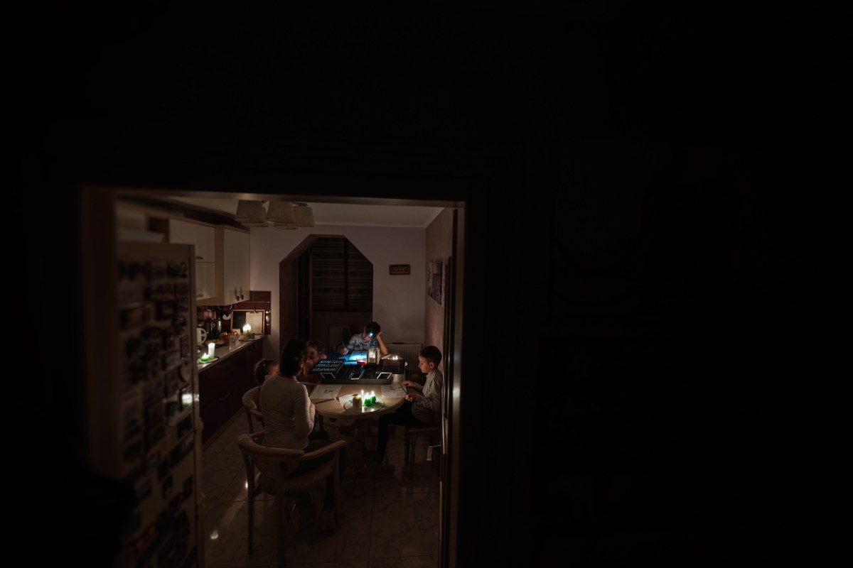 A family gathers around a table with glowing candles and a laptop in a dimly lit kitchen.
