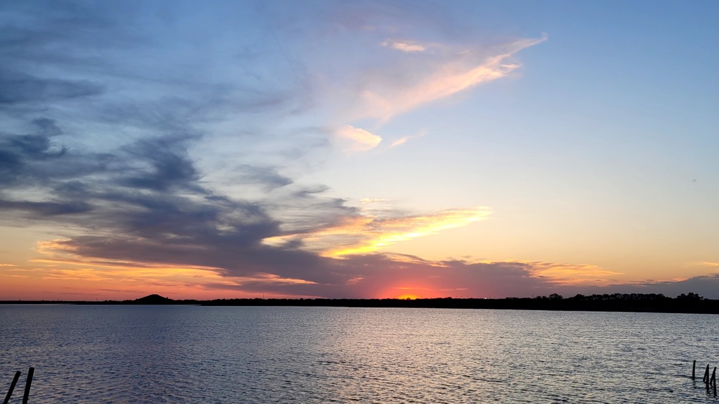 A colorful sunset over a calm body of water with clouds in the sky.