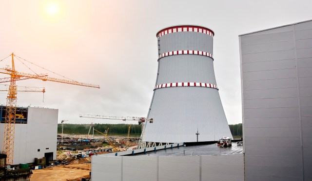 A cooling tower of a nuclear power plant under construction, surrounded by cranes and industrial buildings.