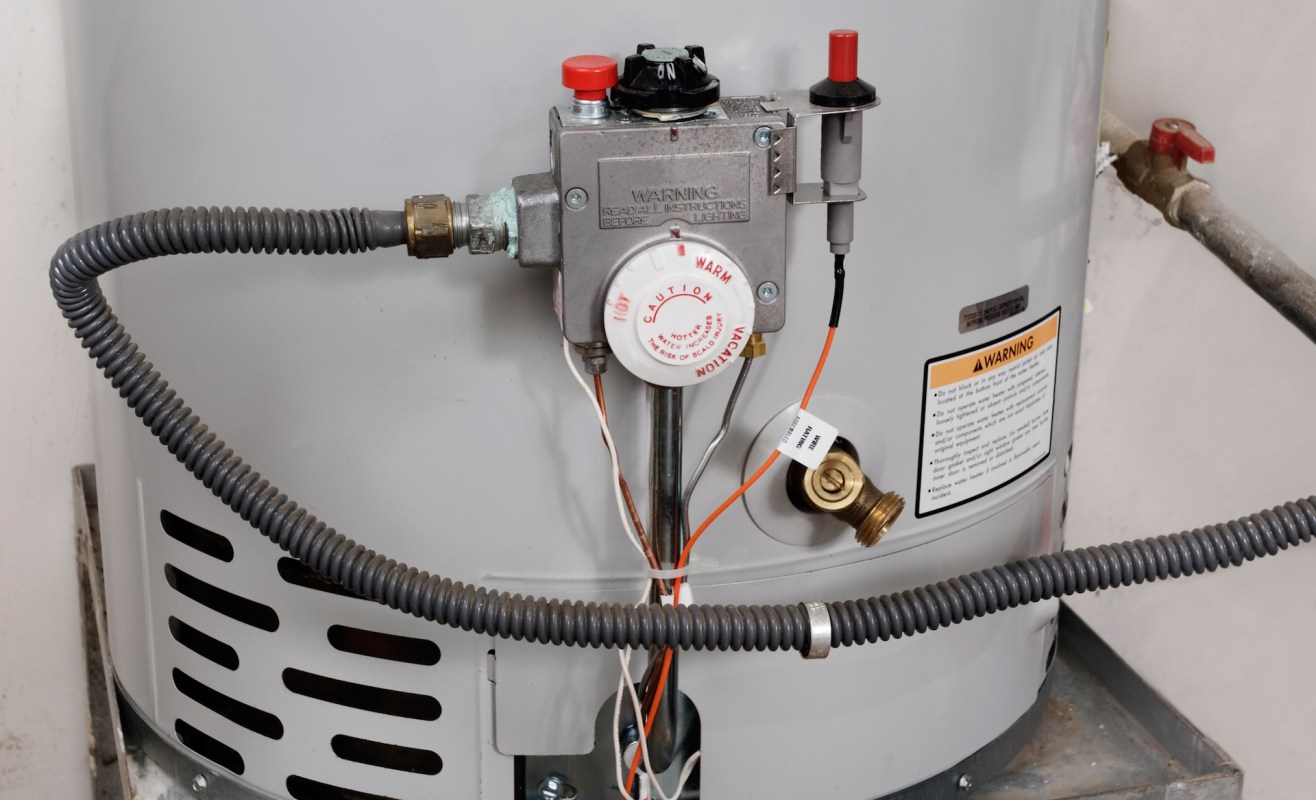 A gas water heater with various pipes, controls, and warning labels.
