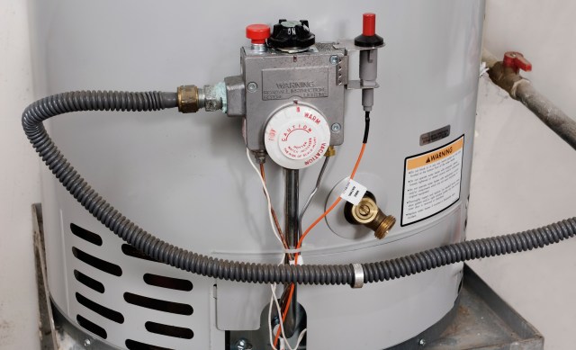 A gas water heater with various pipes, controls, and warning labels.