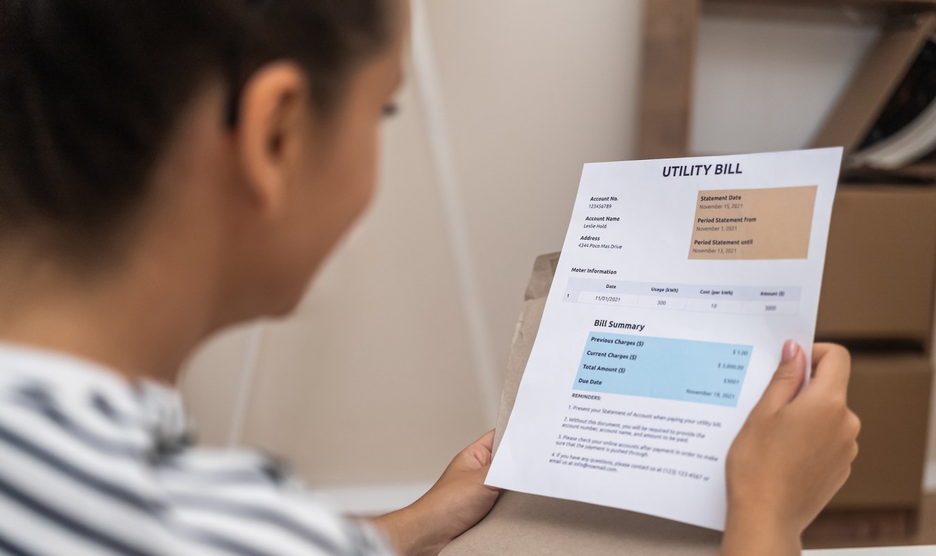 A person holds a utility bill with account details and a bill summary.