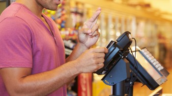 A man crossing his fingers as he pays with a card at a grocery store.